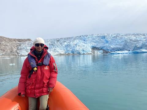 Person in a boat near a glacier wearing a red jacket.