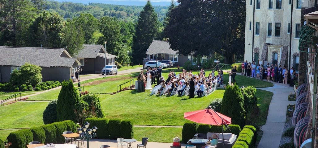 Group of people gathered on a lawn for an outdoor event, possibly a wedding.