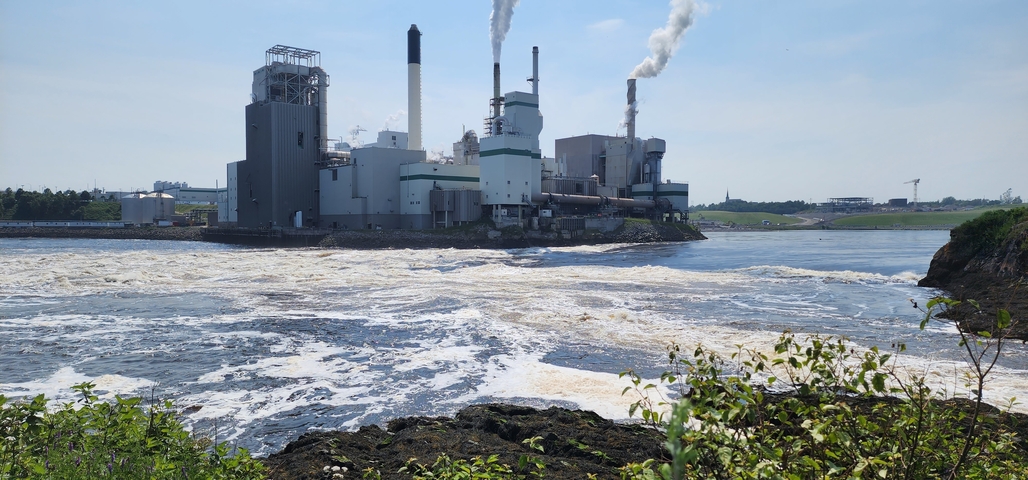 Industrial facility with smokestacks by a river.