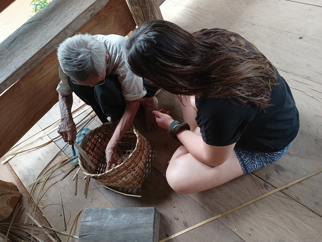 Old person weaving a basket, cultural activity with a younger observer.