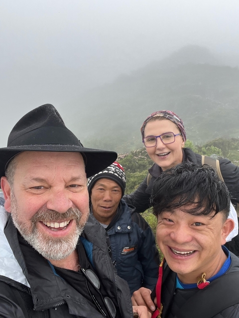 Group selfie on a mountain trail in a misty environment.