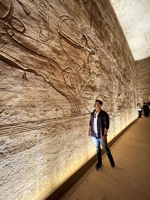       A man standing next to ancient Egyptian hieroglyphs.
  