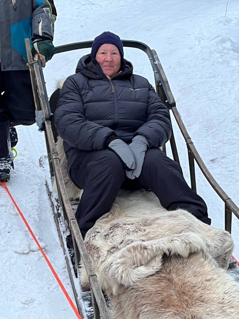 Person sitting in a reindeer sled on snow.