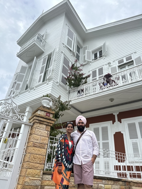 Couple standing in front of a white wooden house with decorative plants.