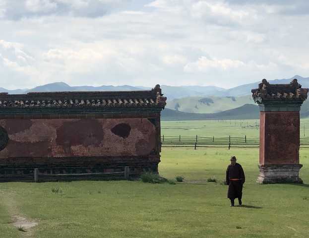 A person walking in front of ancient architecture and mountains.