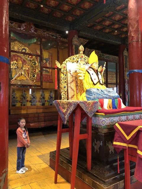 A child next to a richly decorated golden statue indoors.