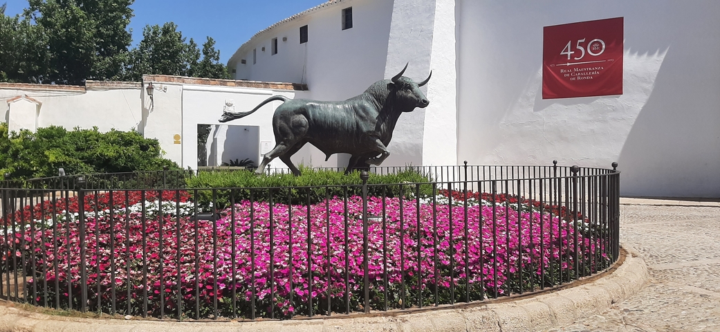       Statue of a bull surrounded by colorful flowers.
  