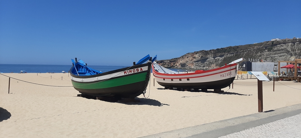       Two traditional boats on the sand with cliffs in the background.
  