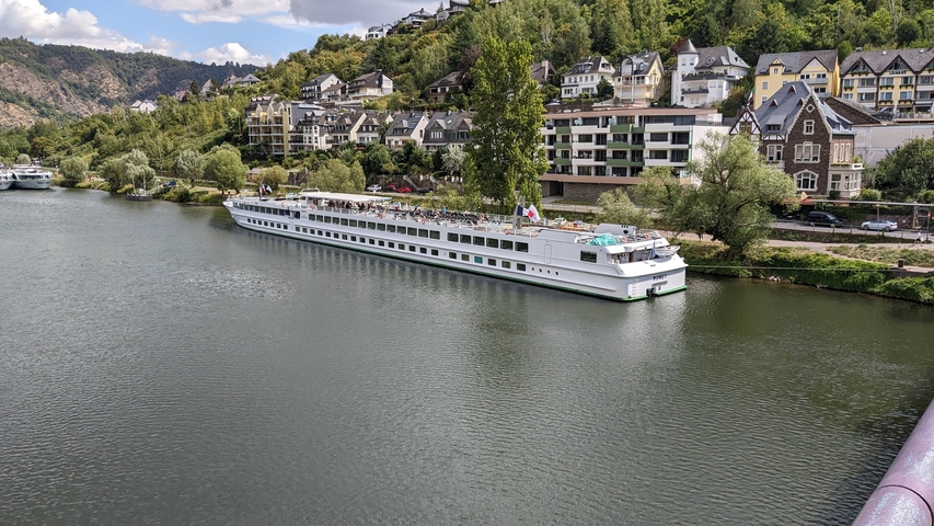 Large cruise ship docked on a river with colorful houses nearby.