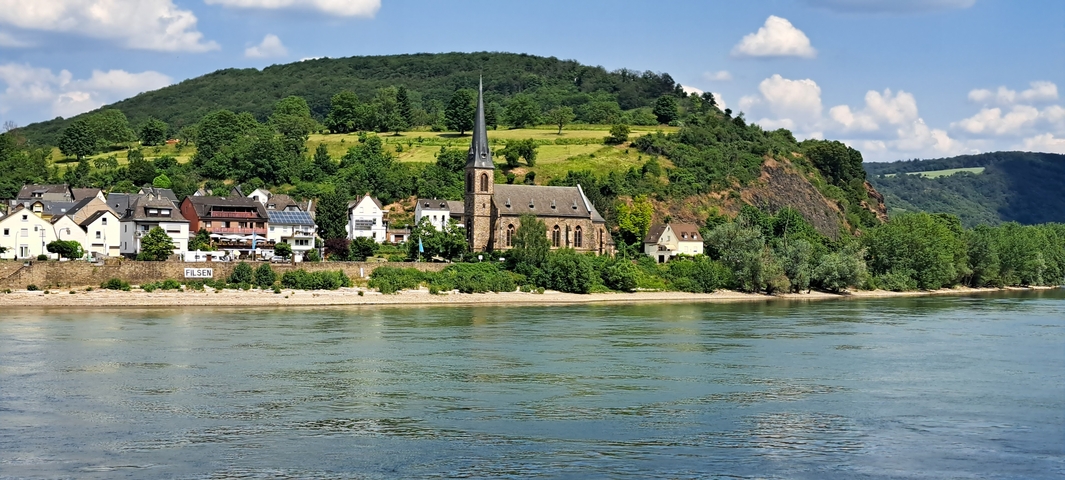 Riverside village with a church and houses on a sunny day.