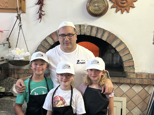       Group photo of kids with a chef in front of a pizza oven.
  