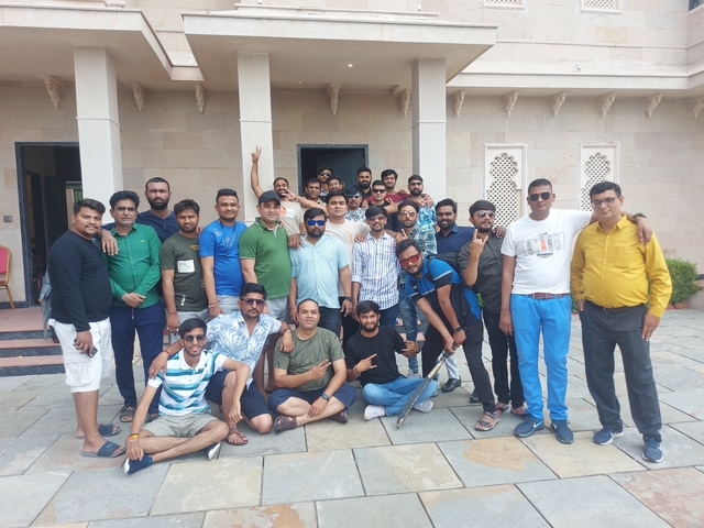 A large group of men pose in front of a building, some kneeling.