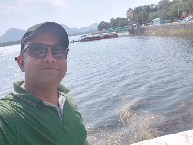 A selfie of a person by the lakeside with mountains in the background.