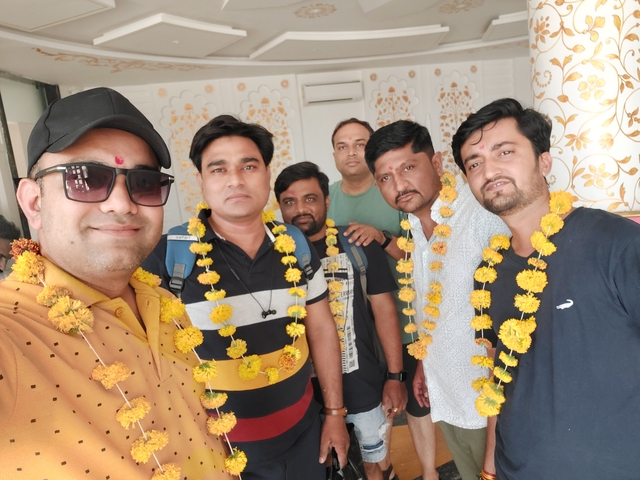 A group of men adorned with garlands poses indoors.