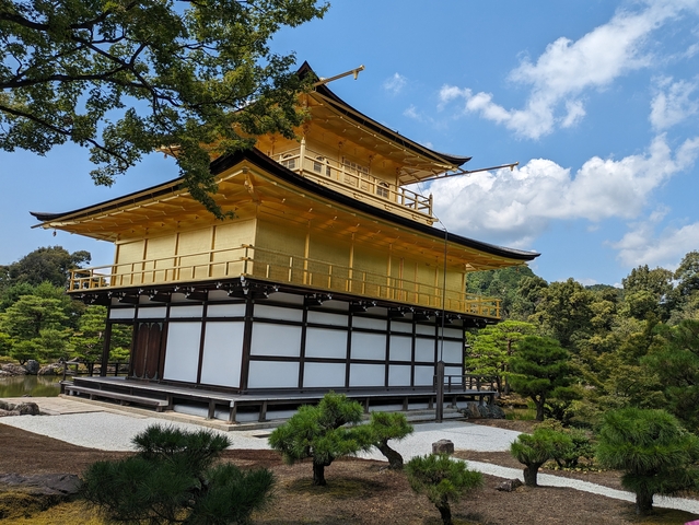       The golden pavilion surrounded by lush trees and a clear blue sky.
  