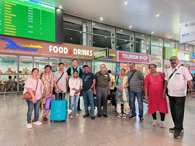 Group of people posing outside a building with various signs in an airport setting.