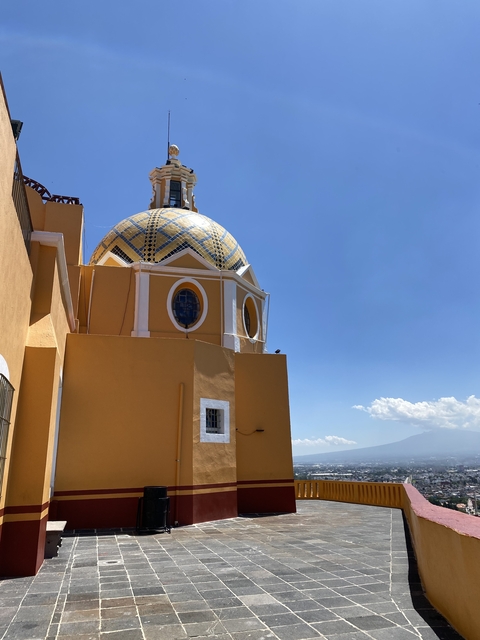       Dome and yellow building with a mountain in the distance under blue sky.
  