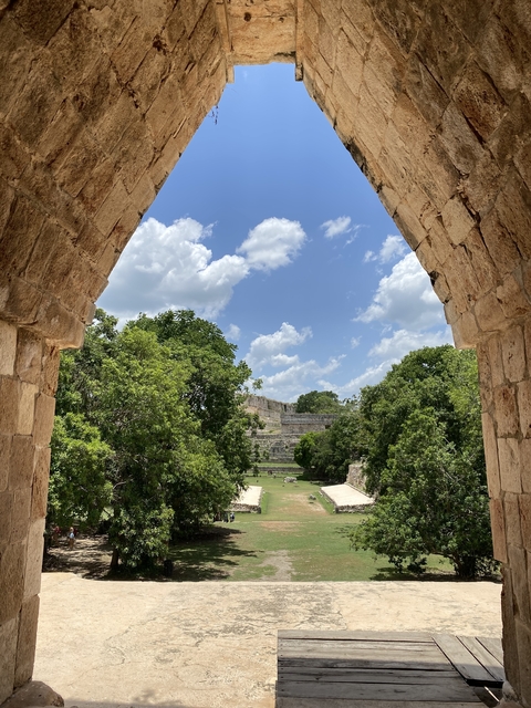 Ancient stone structures and trees under a blue sky with clouds.