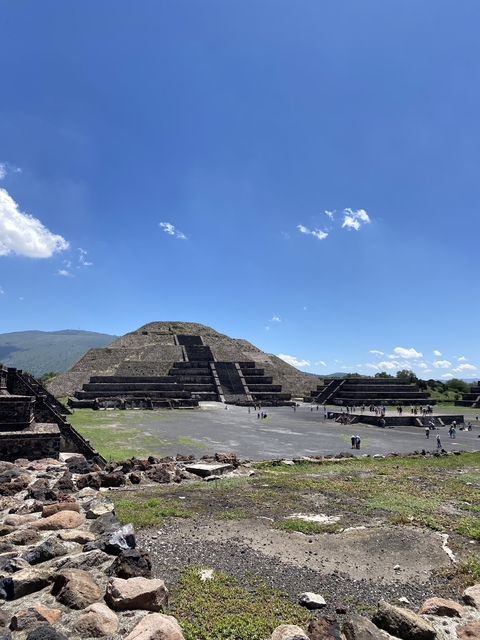 Stepped pyramid with people around, under a blue sky.