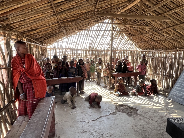 Classroom with children and a teacher in a rustic building.