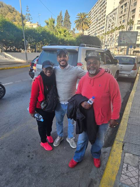 Three people posing for a photo on a city street with cars in the background.