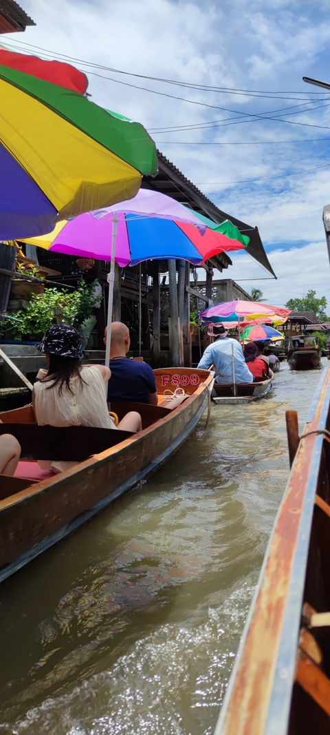 People in boats navigating a narrow river market with vibrant umbrellas.
