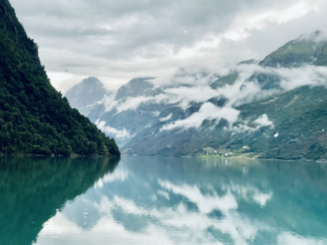 A serene fjord with misty mountains in the background and a calm body of water reflecting the landscape.