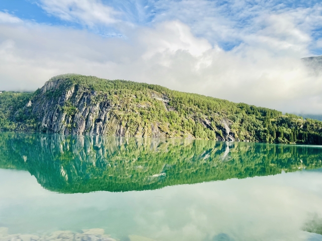 A clear view of a lush green mountain reflecting in the still waters of a lake.