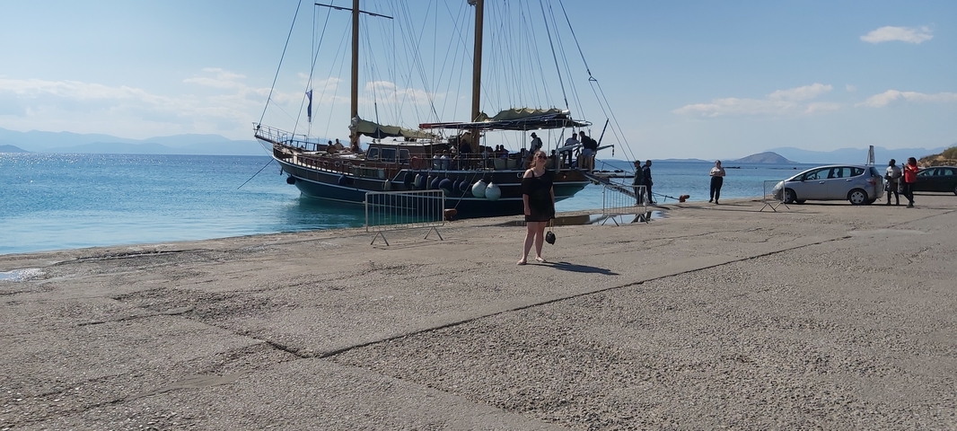 A woman walking on a pier with a sailing ship in the background.