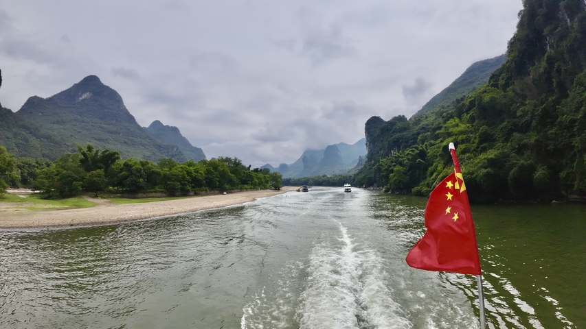 River scene with a national flag on a boat and karst mountains.