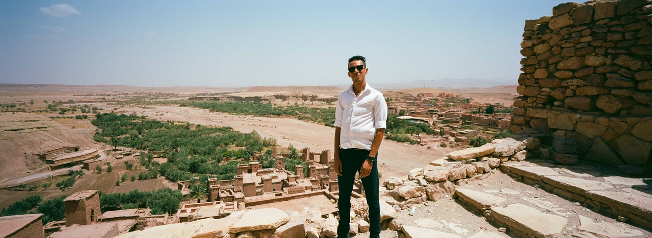       Man in a white shirt standing on ancient ruins overlooking a vast landscape.
  