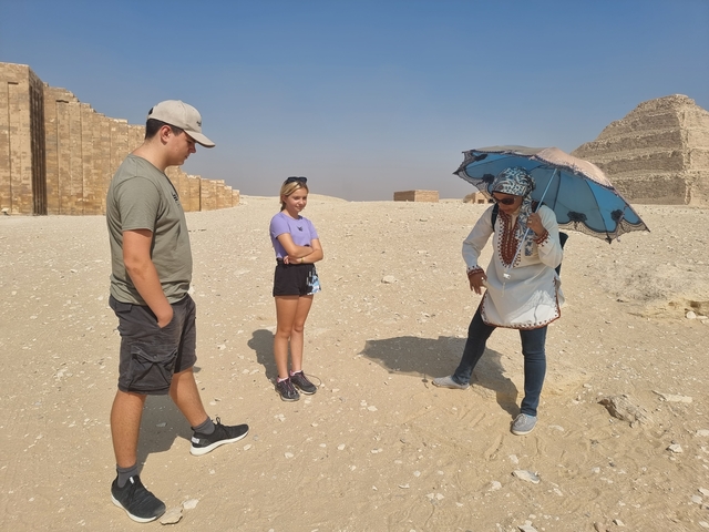 Tour guide showing artifacts on sandy archaeological site with tourists.