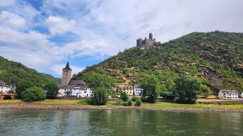       Buildings along a river with a hilltop castle.
  