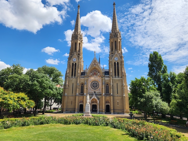       A gothic-style church with tall spires and a park in front.
  