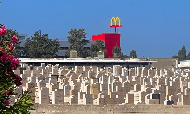 A McDonald's sign over a cemetery with headstones.