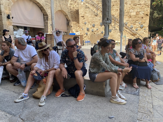      A group of people seated outdoors near a stone structure.
  