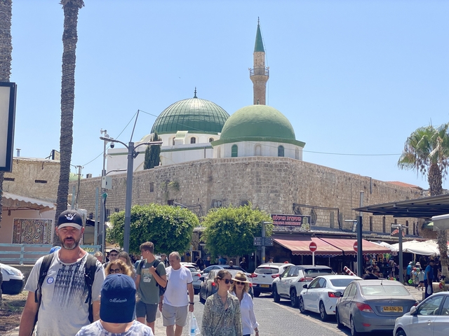      A bustling market scene with a mosque featuring green domes.
  
