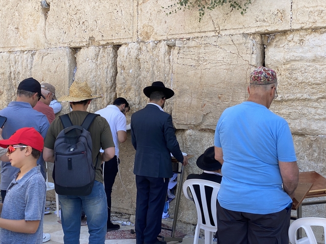       People praying at a historic wall under a sunny sky.
  