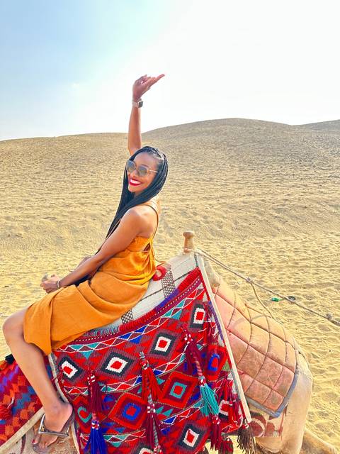 Person riding a camel in a desert setting with traditional decorations.