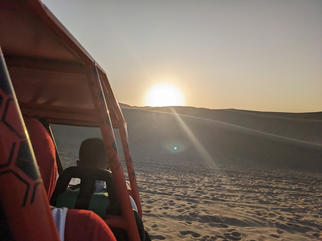       Sunset over dunes with a person in a vehicle.
  