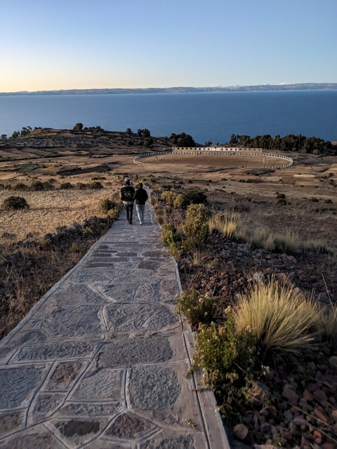       People walking towards a circular structure in a barren landscape.
  