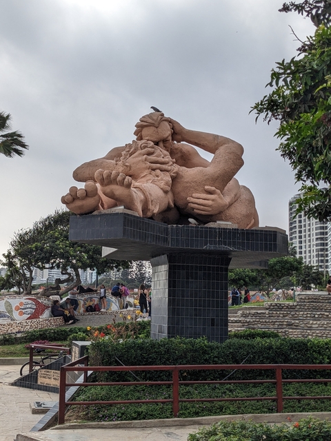 Large statue in an urban park with people around it.