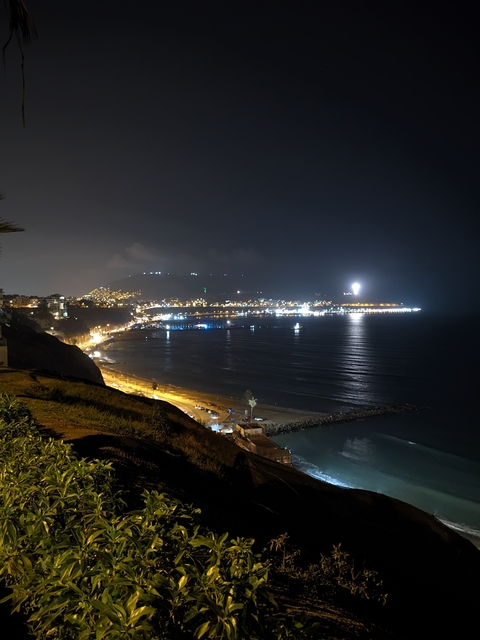       Night view of a coastal city with bright lights reflecting on the water.
  