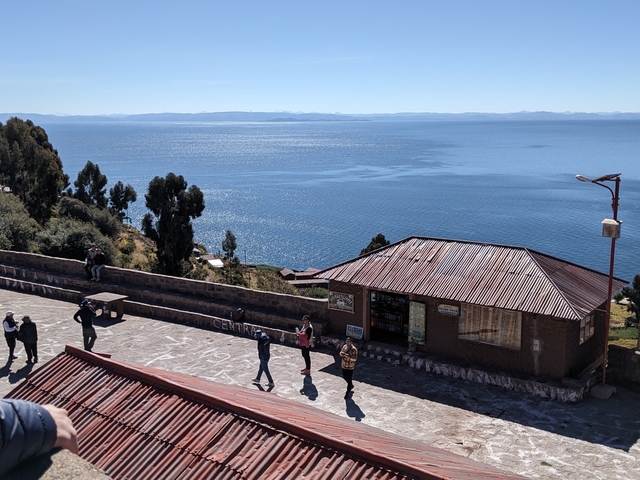       View of a lake with people standing near a building with a corrugated roof.
  