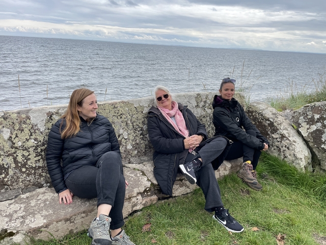 Three women seating on stone benches near the sea.