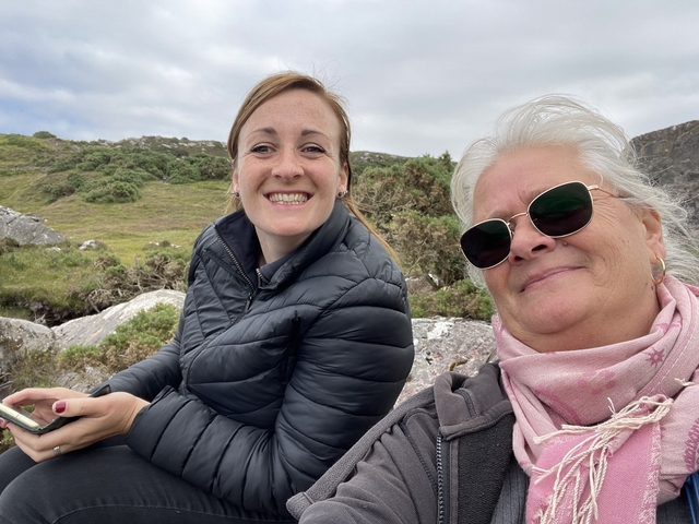       Two women sitting on rocks outdoors, smiling at the camera.
  