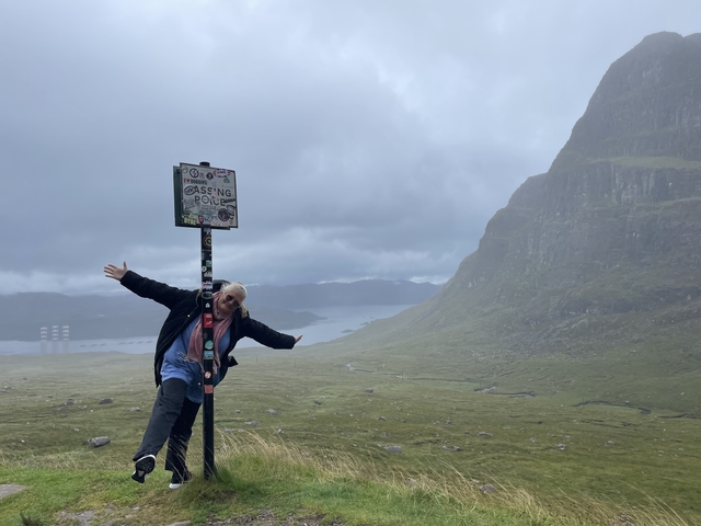      Person playfully posing by a scenic viewpoint sign.
  