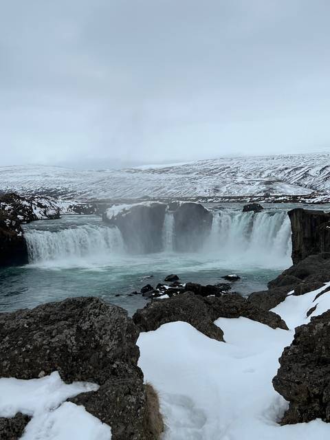       Waterfall cascading down a cliff with snow patches.
  