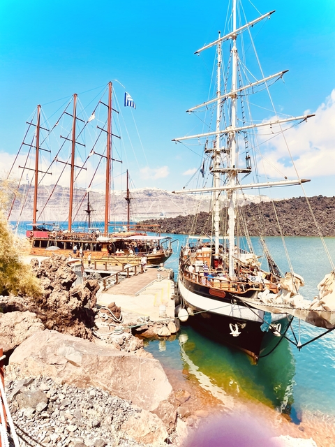 Wooden sailing ships docked at a harbor with a rocky backdrop.