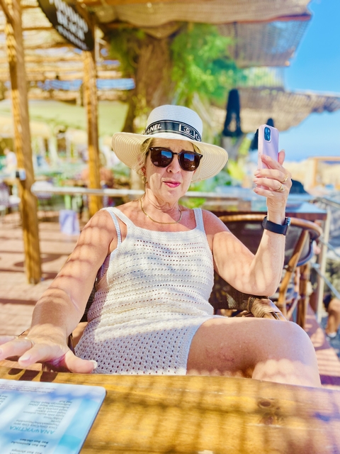 Woman wearing a hat, holding a smartphone, sitting outdoors.